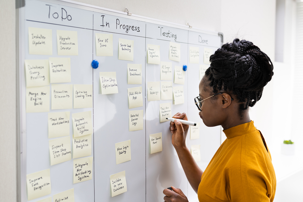 young woman writing on white board used to track progress on a project