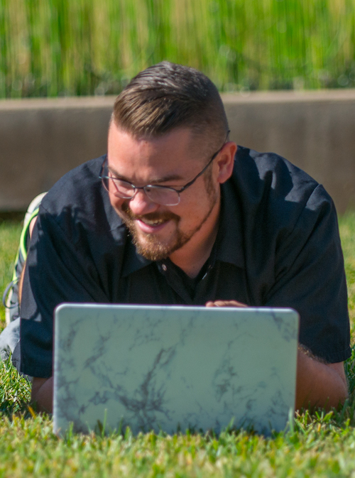 young man using laptop computer while prone on lawn