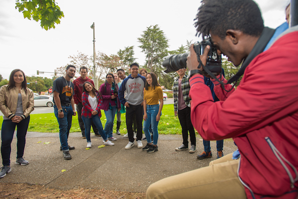 young man with camera photographing group of students