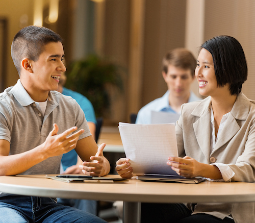 young man talking with young woman who's holding papers at a table